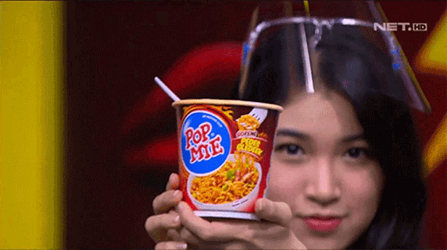 a woman holding a cup of pop mie with a straw in it