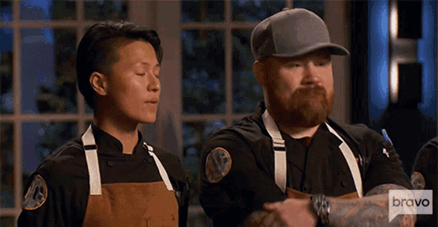 a man with a beard is standing next to a woman wearing an apron with the word bravo on it