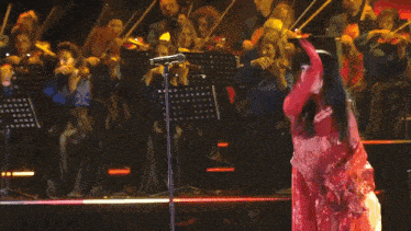 a woman in a red dress is dancing in front of a orchestra