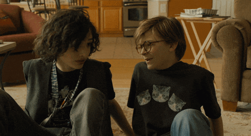 a boy wearing glasses sits next to another boy wearing a black shirt with cats on it