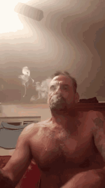 a shirtless man smoking a cigarette in a bedroom