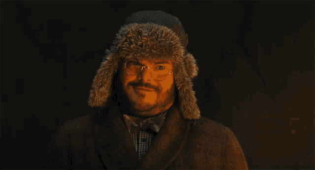 a man wearing a furry hat and glasses looks at the camera