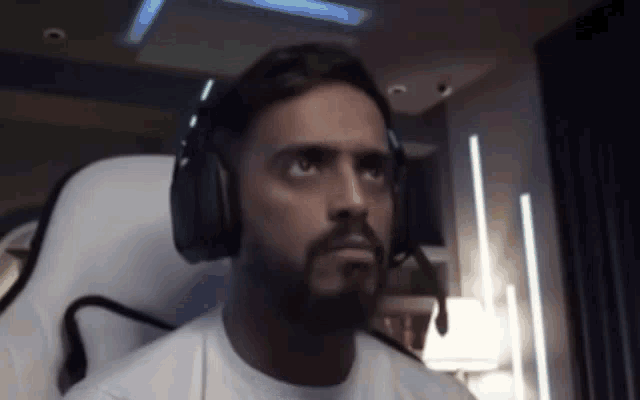 a man with a beard is wearing headphones and a microphone while sitting in a chair .