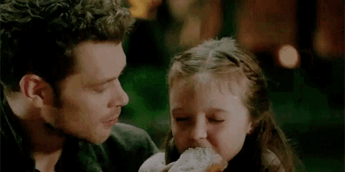 a little girl is eating a sandwich from a man 's hand .