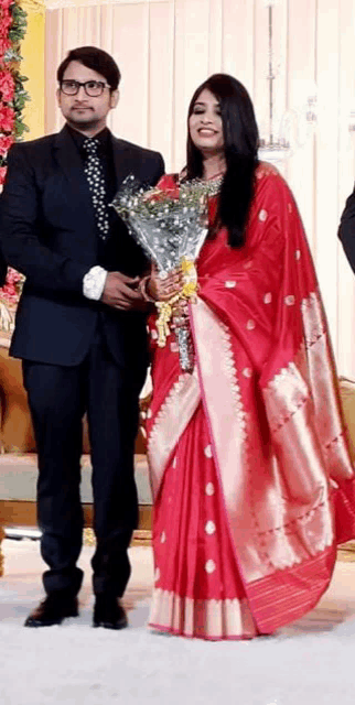a man in a suit and tie is holding a bouquet of flowers next to a woman in a red dress .