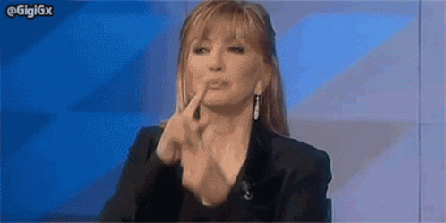 a woman is sitting in front of a blue wall and making a funny face with her hands .