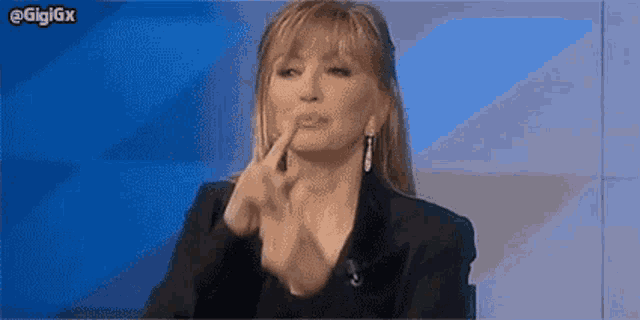 a woman is sitting in front of a blue wall and making a funny face with her hands .