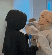 a couple of people are standing next to each other in a room . one of the people is wearing a black hoodie .