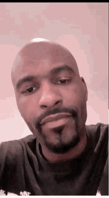 a bald man with a beard wearing a black shirt looks at the camera