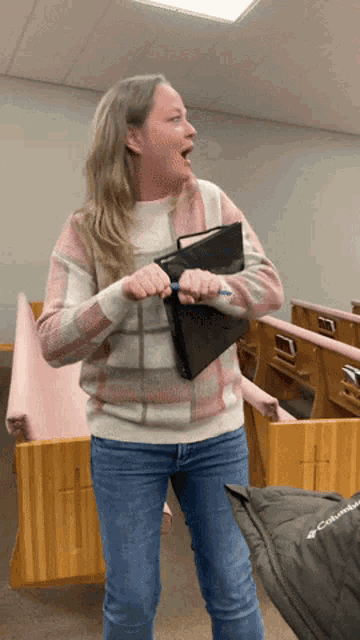 a woman in a plaid sweater and jeans is holding a binder