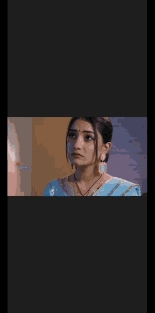 a close up of a woman wearing a blue saree and gold earrings