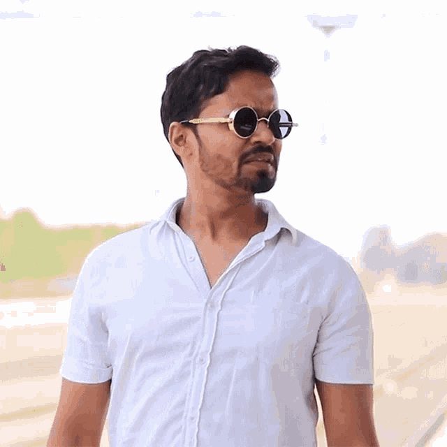 a man wearing round sunglasses and a white shirt is smiling