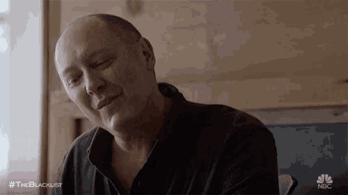 a bald man is smiling with his eyes closed while sitting at a table .