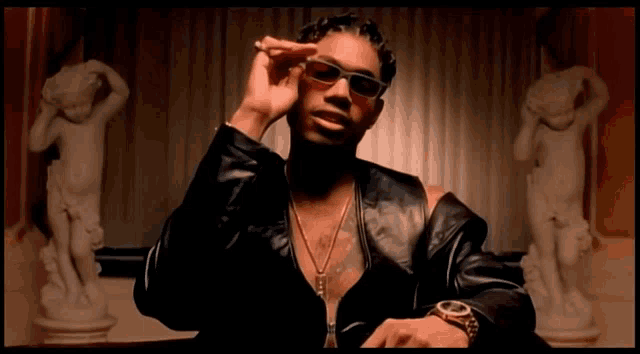 a man wearing sunglasses and a watch is sitting in front of a statue of a woman