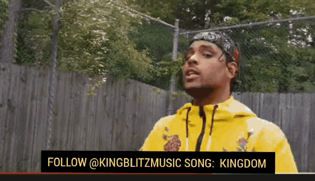 a man wearing a yellow hoodie and a bandana is standing in front of a fence .