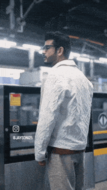 a man wearing glasses and a white jacket is standing in front of a sign that says @ jayson125