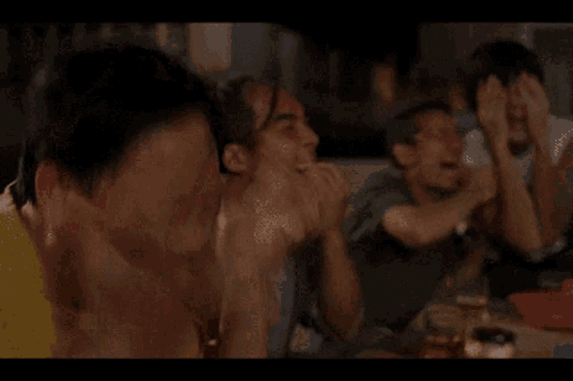 a group of people sitting around a table with their hands on their heads