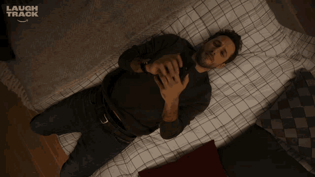 a man is laying on a bed looking at his phone with a laugh track logo in the background