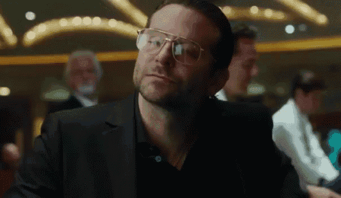 a man wearing glasses and a black suit is sitting at a table in a casino .