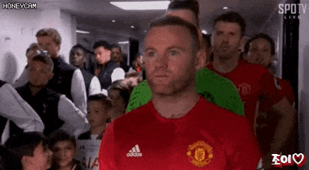 a man in a red shirt is standing in front of a crowd of people in a dressing room .