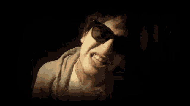 a man wearing sunglasses makes a funny face in the dark