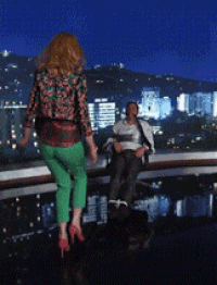 a woman in green pants is walking towards a man in a tie