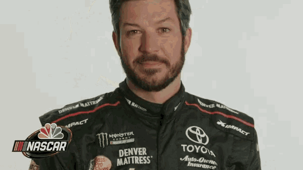 a man with a beard is wearing a racing uniform and a nascar logo .