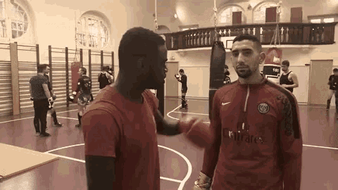 a man in a red shirt with the word fly emirates on it is shaking hands with another man on a basketball court .