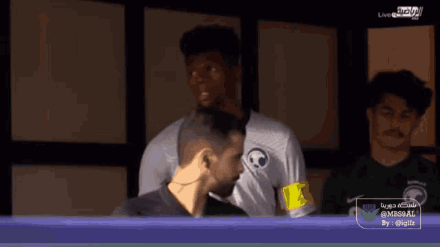 a man in a white shirt with a soccer ball on it stands next to a man in a green shirt