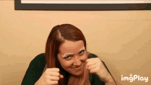 a woman with red hair and white eyebrows is making a funny face with her fist in the air .