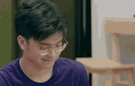 a young man wearing glasses is smiling while sitting at a table .
