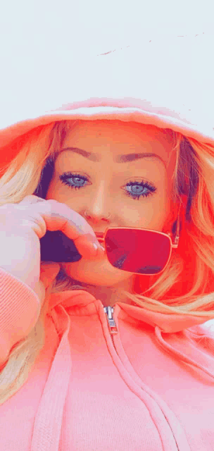a woman wearing a pink hoodie and red sunglasses takes a selfie