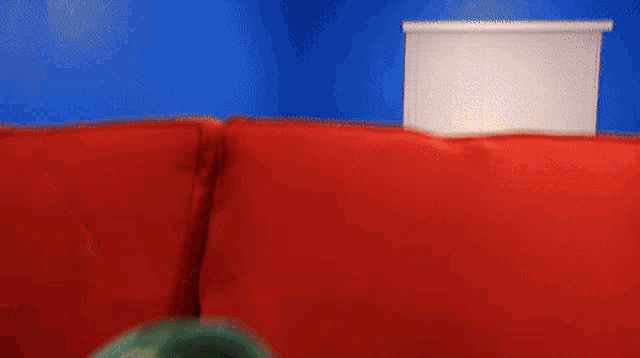 a puppet is sitting on a red couch with its mouth open