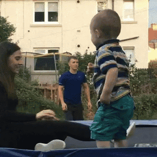 a little boy is standing on a trampoline while a woman sits on it