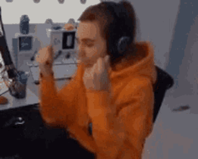 a man in an orange hoodie is wearing headphones and making a funny face .