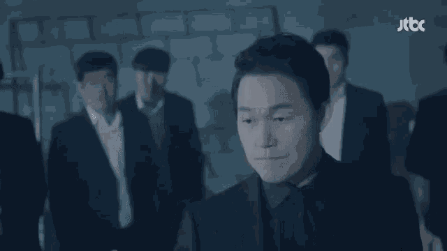 a man in a black suit and tie is standing in front of a group of men .