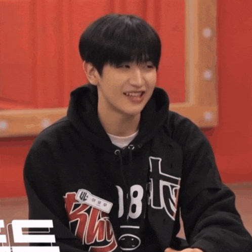 a young man wearing a black hoodie with the number 18 on it is smiling