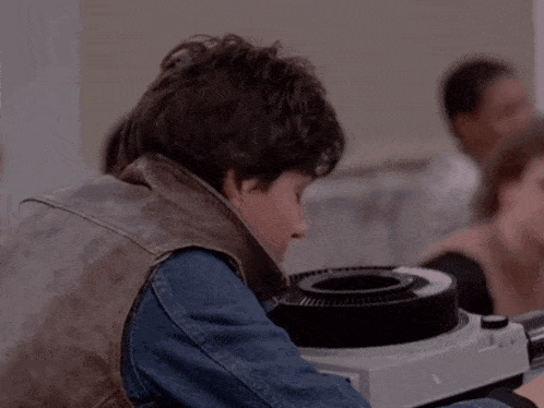 a young man wearing a leather vest is sitting in front of a slide projector