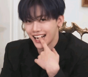 a young man in a black suit is holding his finger to his mouth