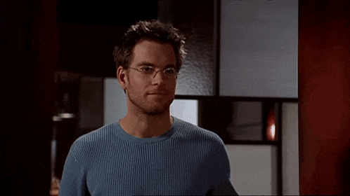 a man wearing glasses and a blue sweater is looking at the camera