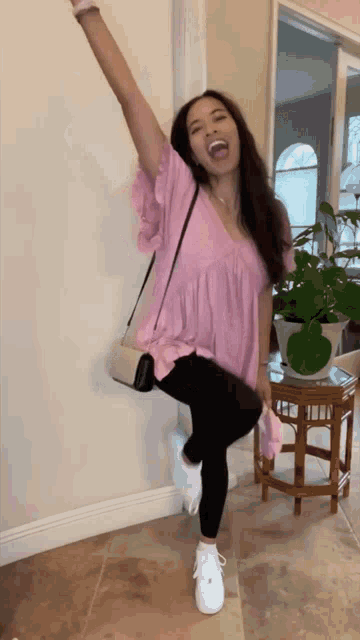 a woman in a pink top and black leggings is standing on one leg with her arm in the air .