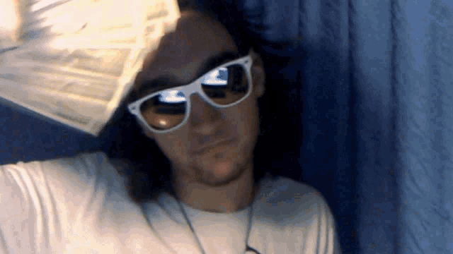 a man wearing sunglasses and a white shirt holds a stack of money over his head