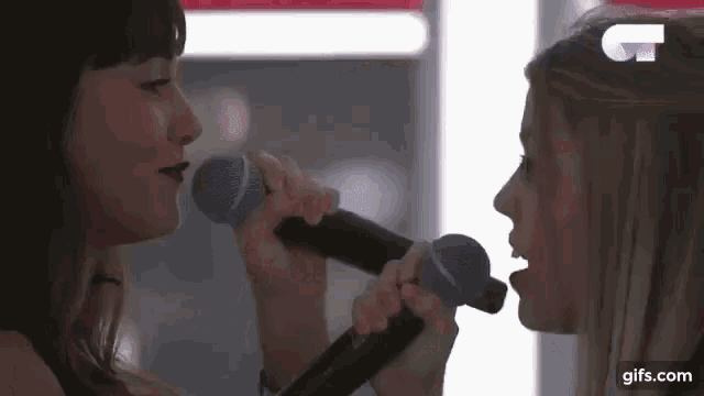 two women are singing into microphones together .