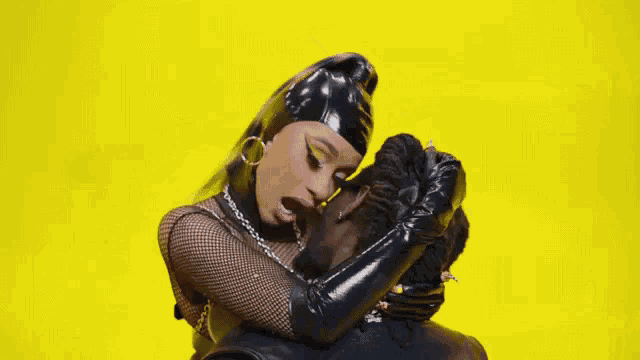 a woman in black latex gloves is sitting on a man 's lap and licking his face .