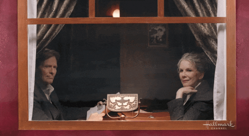 a man and a woman sit at a table in front of a hallmark channel sign