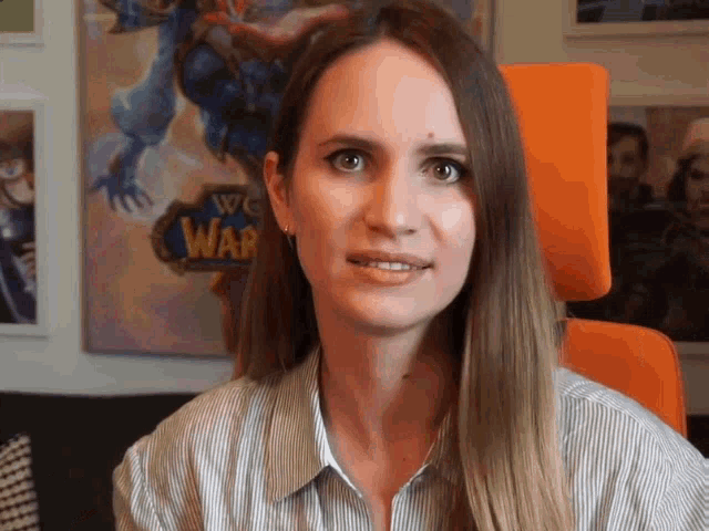 a woman sitting in an orange chair with a world of warcraft logo behind her