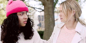 two women are standing next to each other in front of a tree and talking .