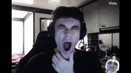 a man wearing headphones is making a funny face while sitting in front of a computer screen that says vidu on it
