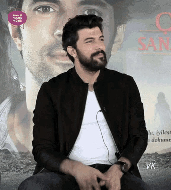 a man with a beard is sitting in front of a poster with the word san on it