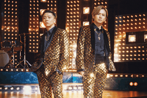 two men in gold suits are standing on a stage in front of a drum set